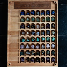 Load image into Gallery viewer, A wooden poly-die storage board with a carved top plaque reading 'Nixier's Outfitter,' holding rows of colorful polyhedral gaming dice on a dark background.