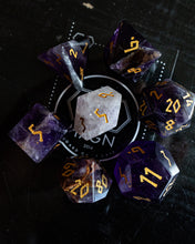 Load image into Gallery viewer, A set of translucent purple and smoky gray polyhedral gaming dice with gold numbers, arranged around a white circular logo on a dark surface.