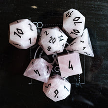 Load image into Gallery viewer, A set of translucent pale pink polyhedral gaming dice with black printed numbers, arranged on a dark textured surface.