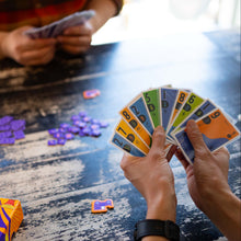 Load image into Gallery viewer, Two people playing a card game with colorful cards on a table, one of which has a 'SCOUT' box.