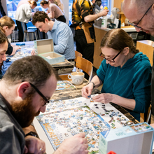 Load image into Gallery viewer, People working on a puzzle together at a table with a casual setting.