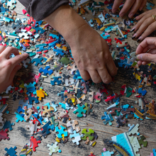 Load image into Gallery viewer, People working on a puzzle with various colored pieces on a wooden surface