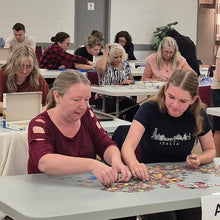 Load image into Gallery viewer, Group of people sitting at tables in a large room, solving puzzles.