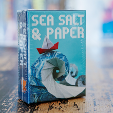 Load image into Gallery viewer, Sea Salt & Paper product packaging with a stylized wave design on a wooden surface.