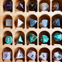 Load image into Gallery viewer, A wooden tray with multiple curved compartments holding assorted polyhedral dice. The dice come in many colors and finishes, including translucent, metallic gold, black, and green marbled patterns, arranged in a neat grid.
