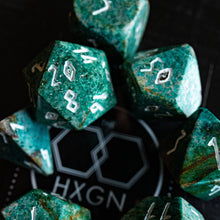 Load image into Gallery viewer, A set of green mottled polyhedral dice with white numbering, arranged on a black surface around a circular black logo that reads HXGN.
