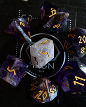 Load image into Gallery viewer, A set of translucent purple and smoky clear polyhedral gaming dice with gold-colored numbers, arranged in a circle around a central light gray translucent d6 on a black background with a circular logo.

