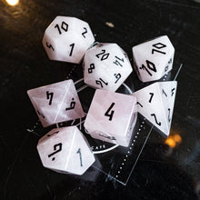 Load image into Gallery viewer, A set of translucent pale pink polyhedral gaming dice with black printed numbers, arranged on a dark reflective tabletop.

