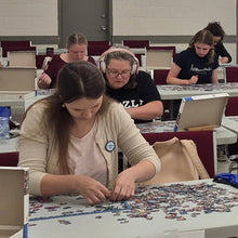 Load image into Gallery viewer, Group of people sitting at tables with laptops in a large room.
