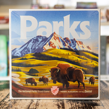 Load image into Gallery viewer, Board game box titled 'Parks' with a mountain and bison design on a wooden surface.
