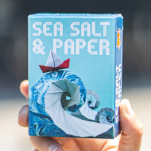 Load image into Gallery viewer, Hand holding a 'Sea Salt &amp; Paper' product packaging with a stylized design.
