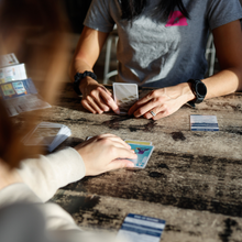 Load image into Gallery viewer, Two people playing cards at a wooden table
