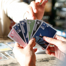 Load image into Gallery viewer, One person holding playing cards while another person's hand reaches out to pick a card with a blurred background
