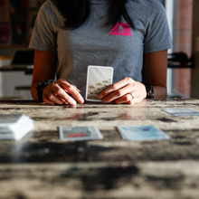 Load image into Gallery viewer, Person holding playing cards at a table 
