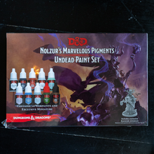 Load image into Gallery viewer, Dungeons &amp; Dragons Nolzur's Marvelous Pigments Undead Paint Set box with 10 paint bottles and a miniature figure shown on a dark reflective surface.
